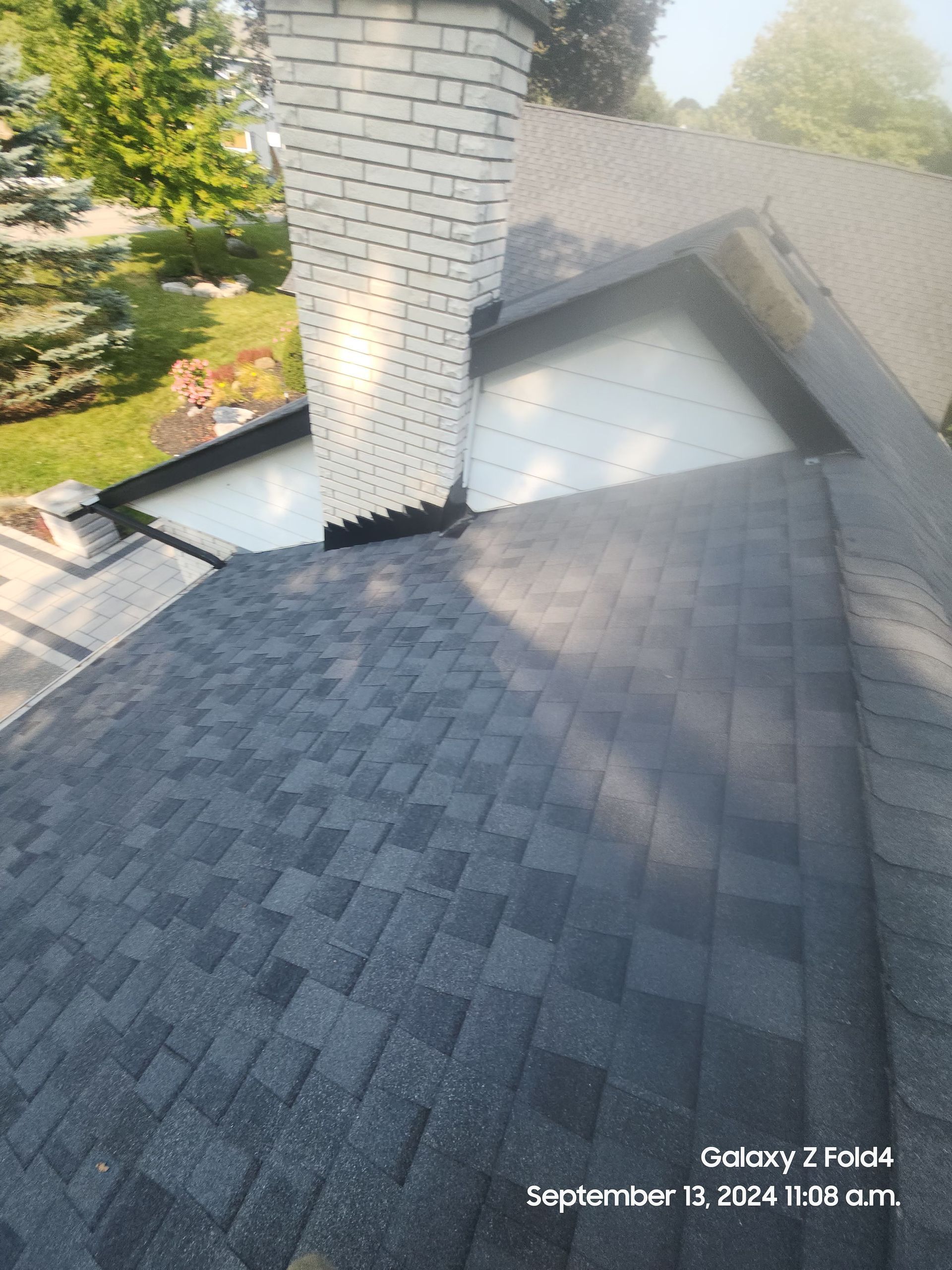 Dark shingle roof with a white brick chimney beside a skylight, viewed from above.