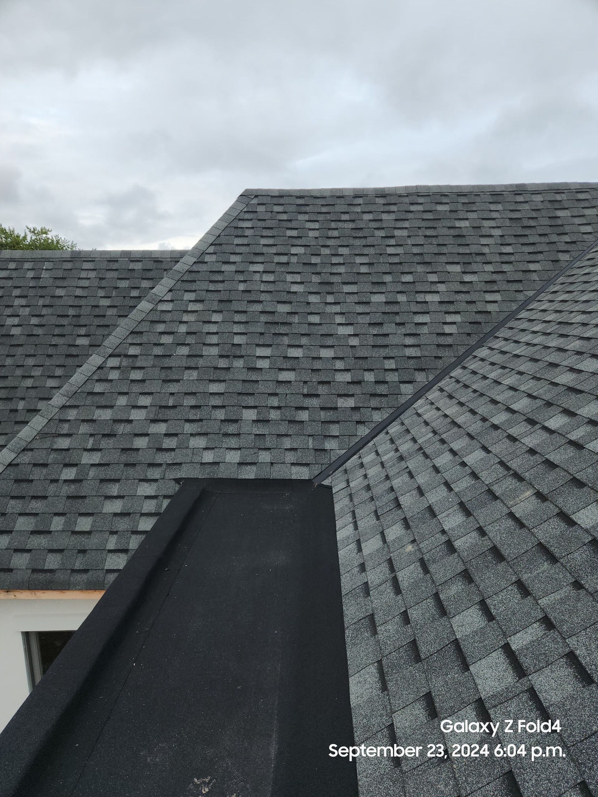 Gray shingled roof with dark ridge vent under a cloudy sky