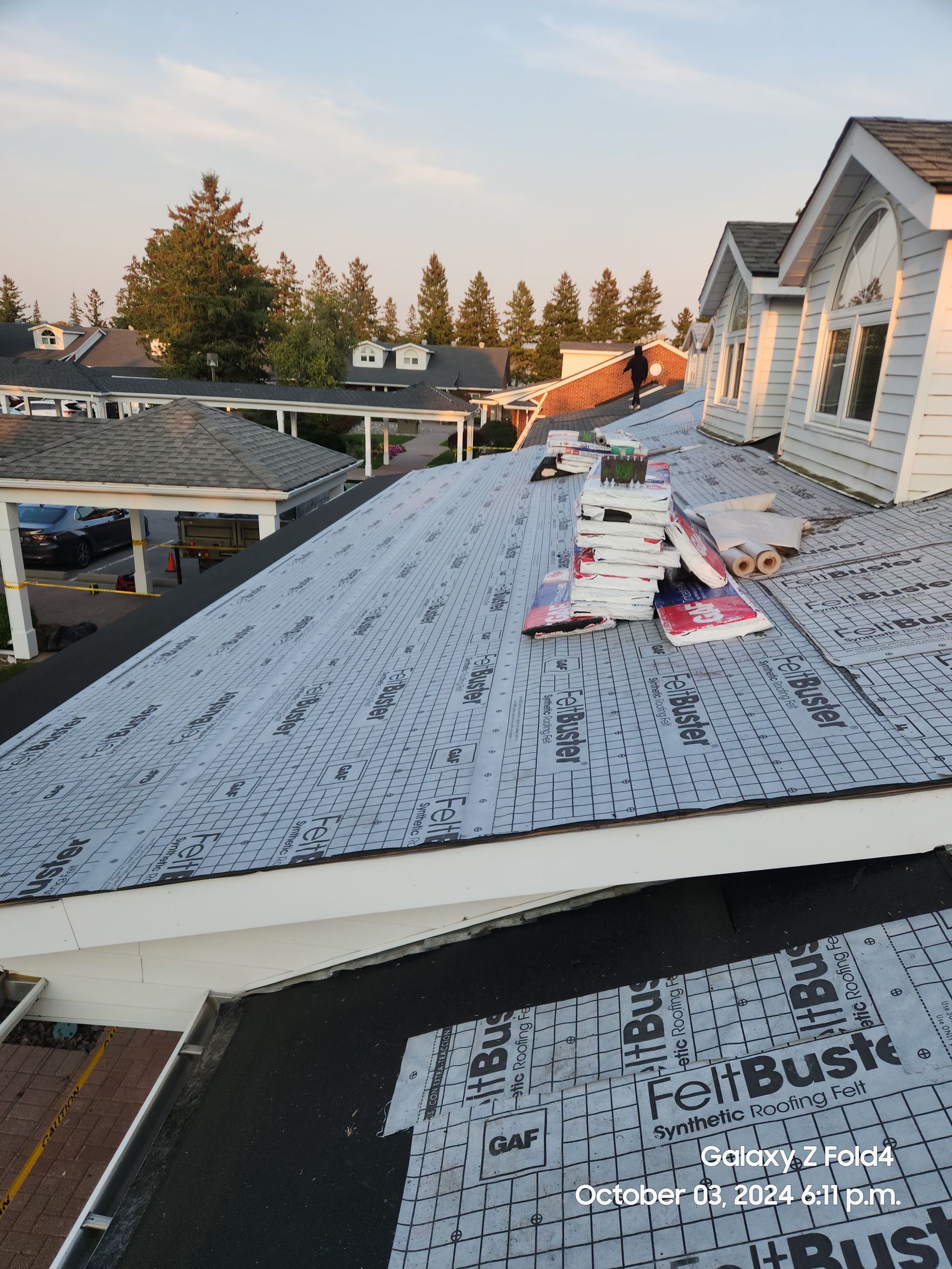 Workers installing roofing underlayment on a sloped house roof at sunset