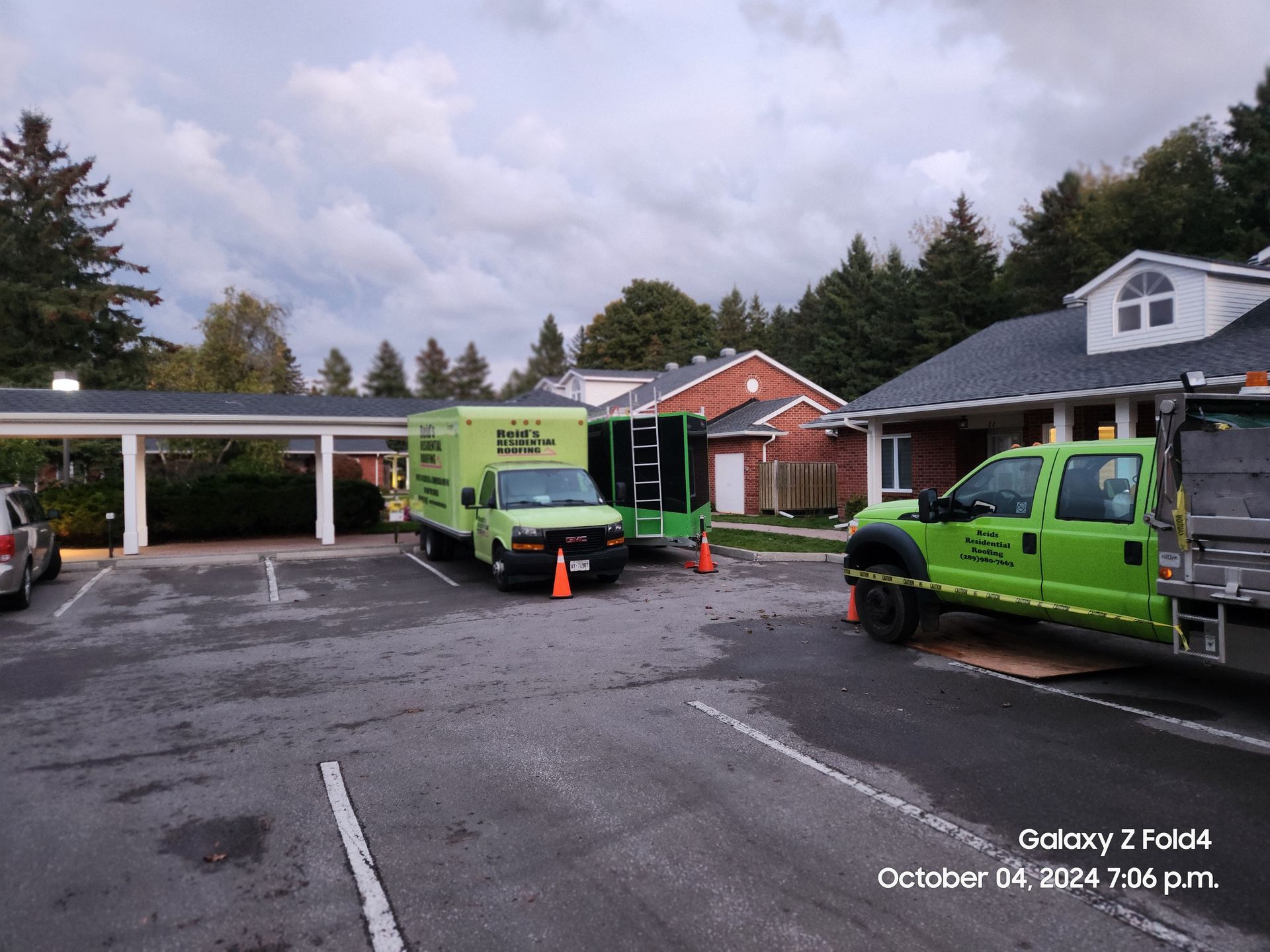 Green work trucks and a trailer in a wet parking lot outside a brick building under cloudy skies