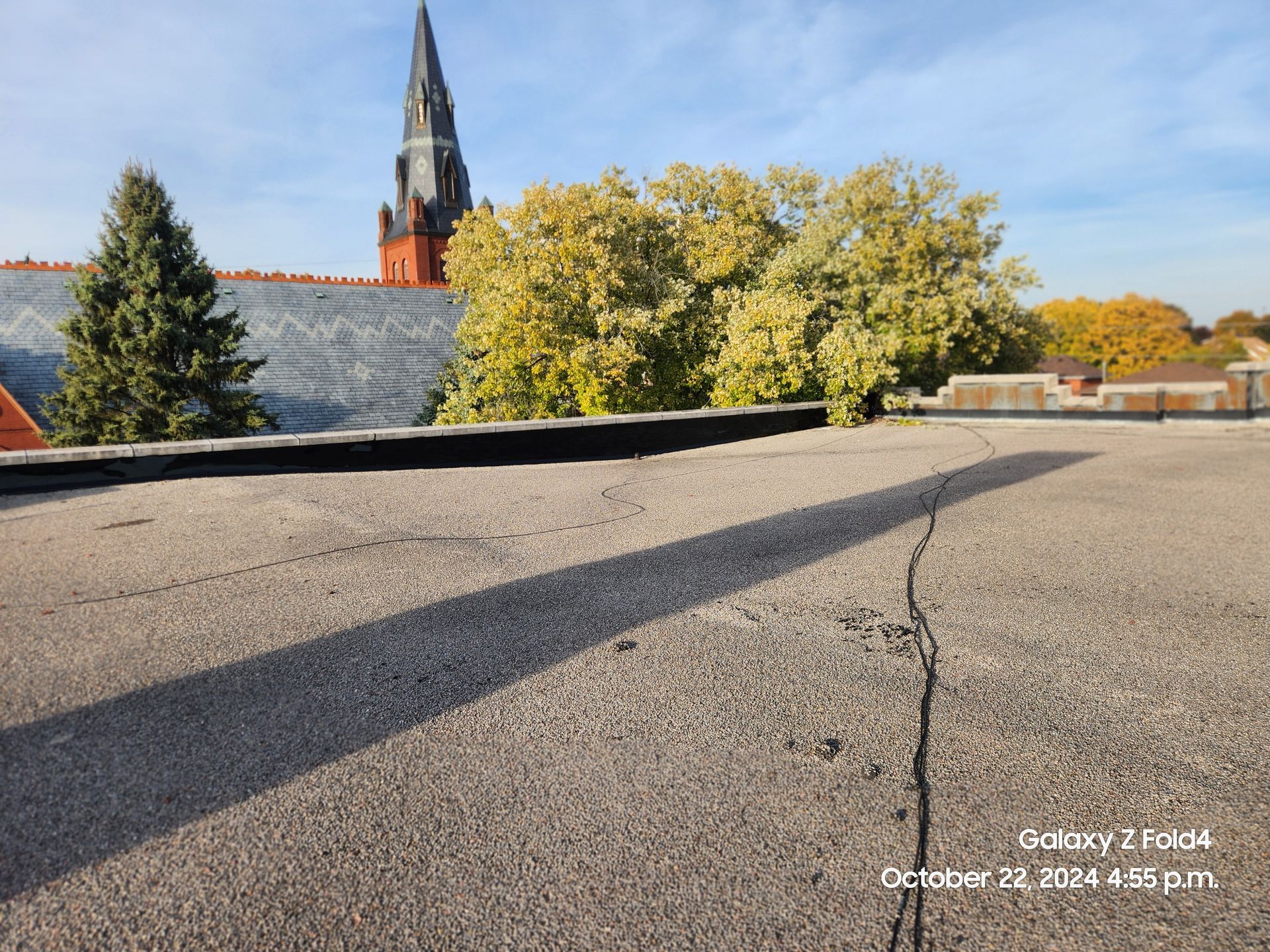 Rooftop with gravel surface, church steeple, and autumn trees under a blue sky