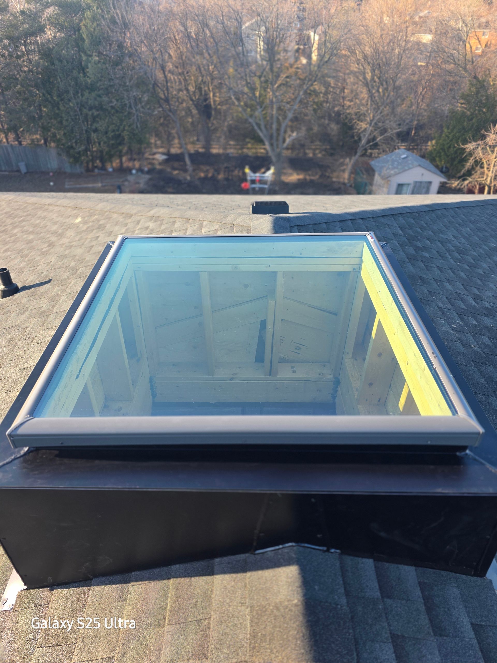 Skylight window on a shingled roof with trees in the background
