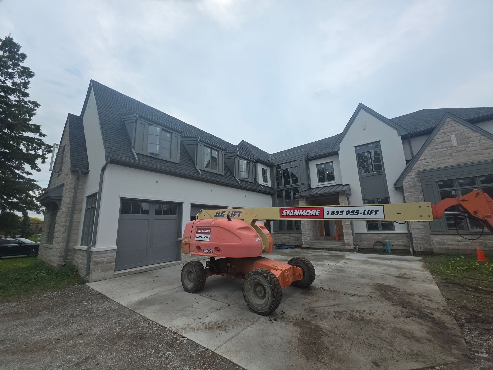 Orange boom lift in front of a new house under construction with gray siding and a driveway.