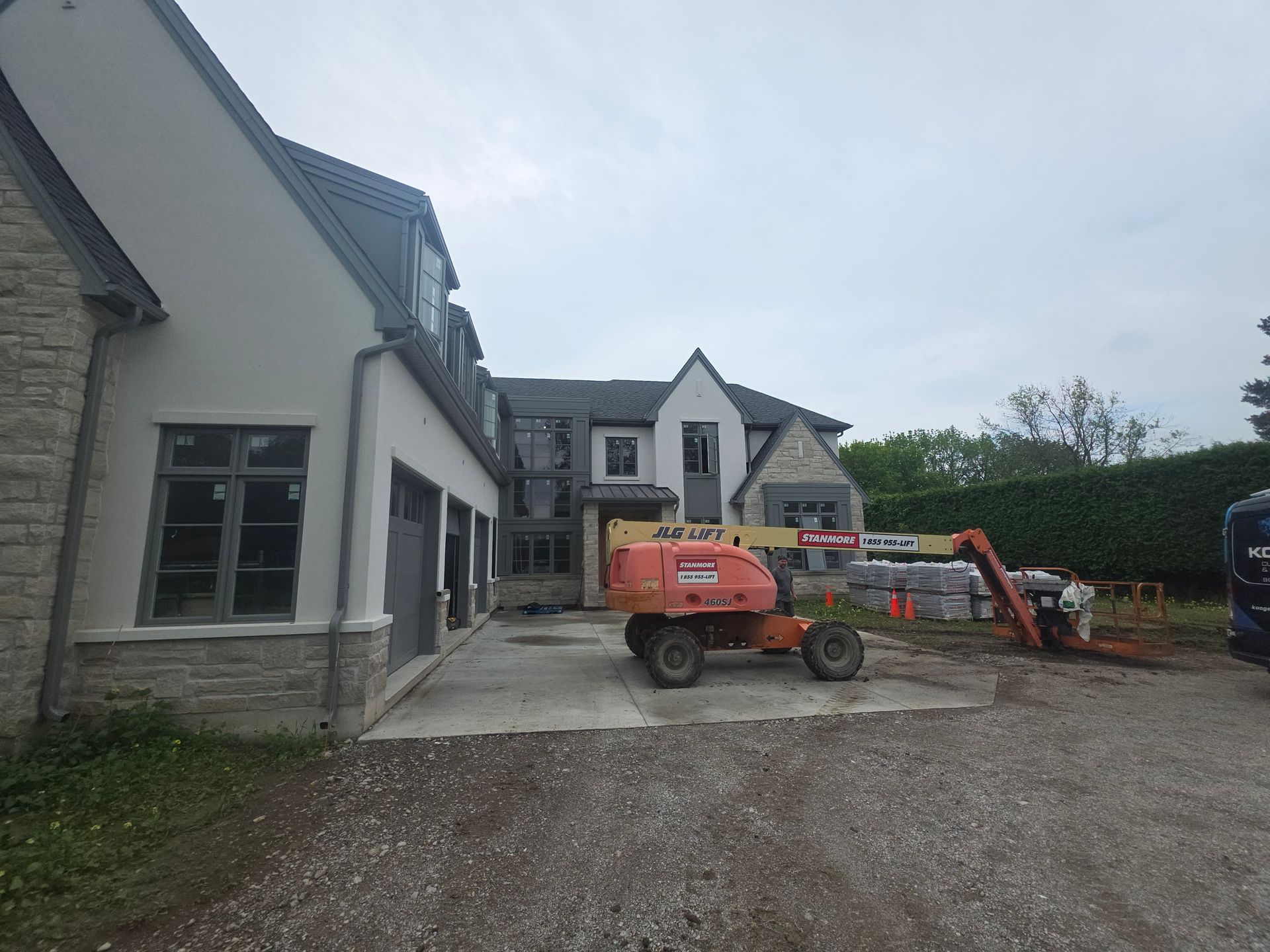 Construction site with house exterior, orange excavator, and gravel driveway under cloudy sky