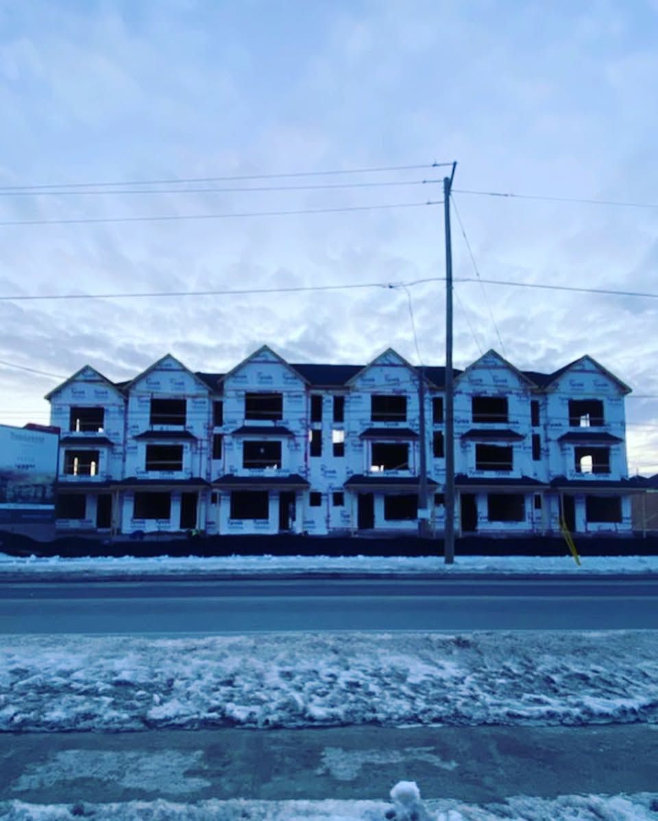 Row of unfinished townhouses across a snowy street under a cloudy sky