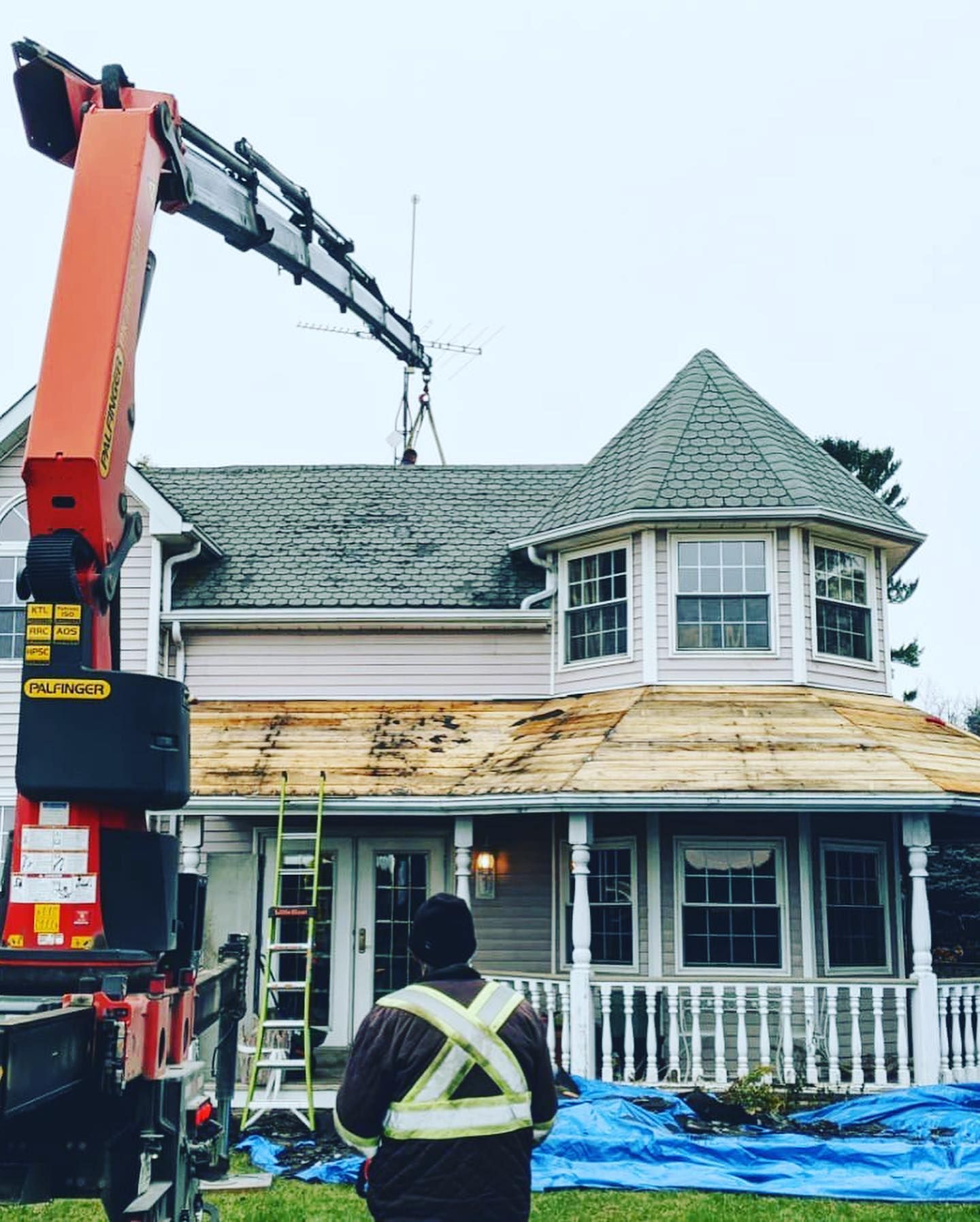 Construction crew using a crane to repair the roof of a white house with gray shingles in wet weather