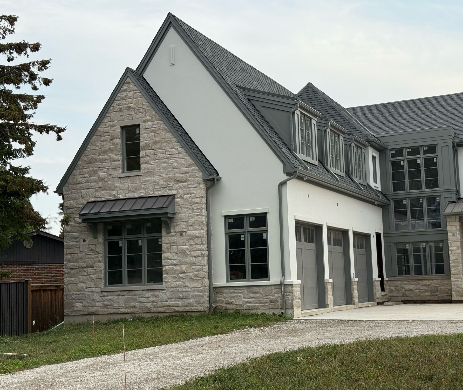 Modern gray stone house with steep roof, dormer windows, and a gravel driveway