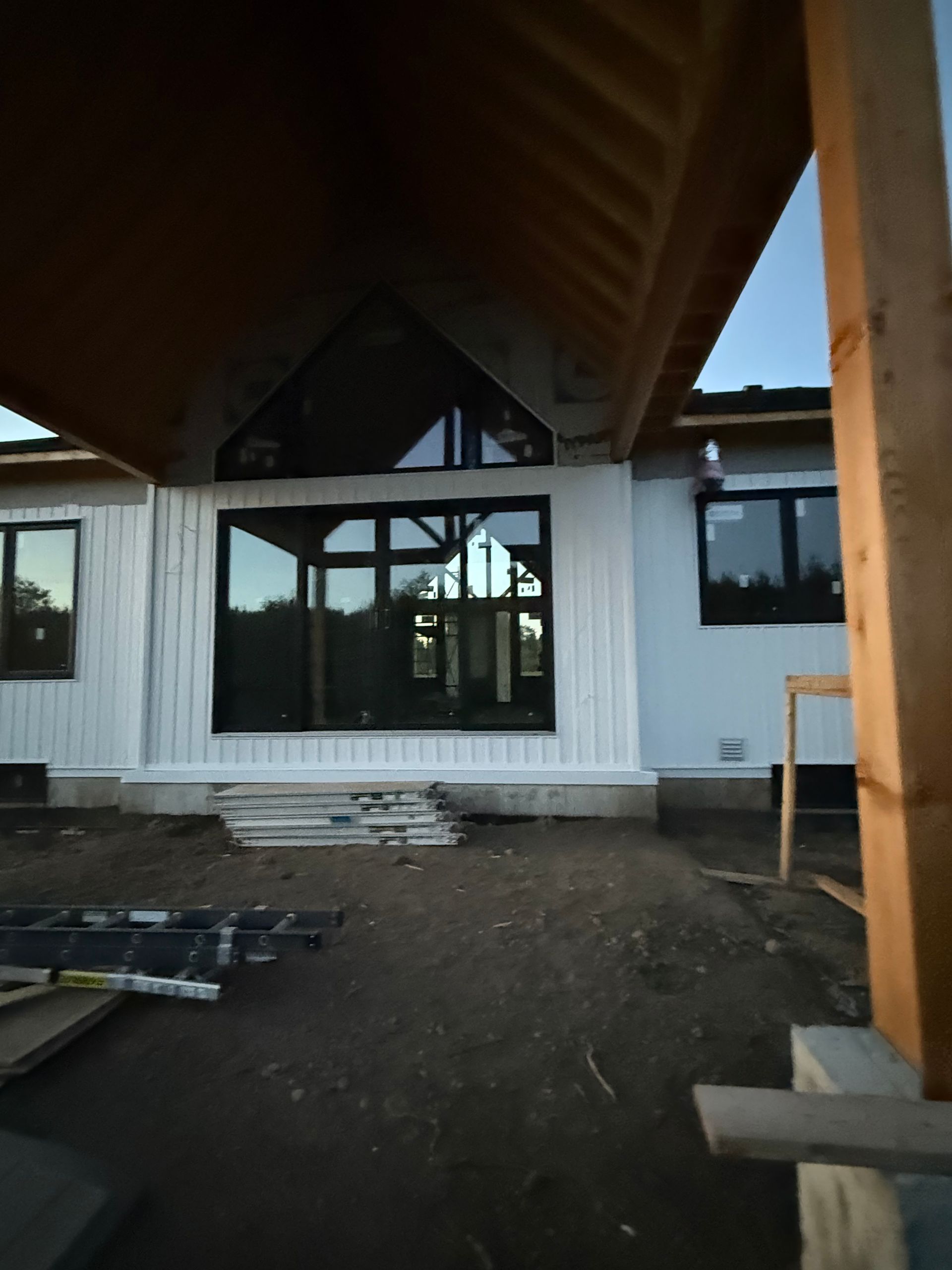Front of a modern house under construction, with large windows and unfinished yard.