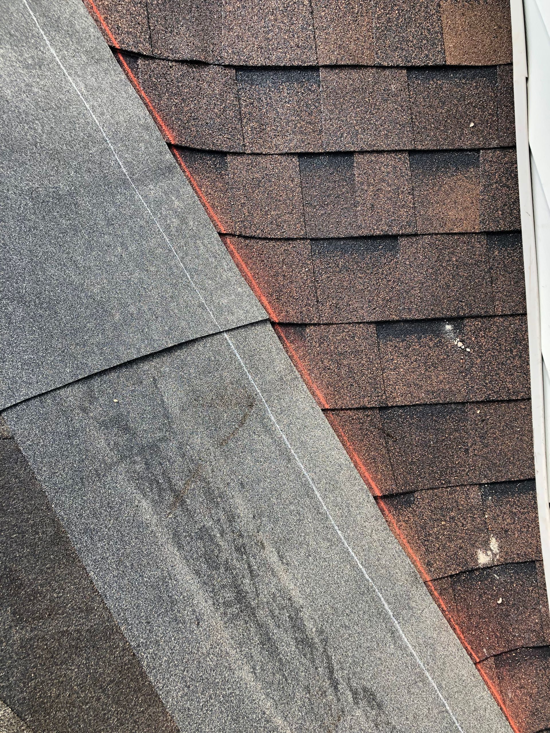 Close-up of a roof seam with gray and brown asphalt shingles and red flashing along the edge