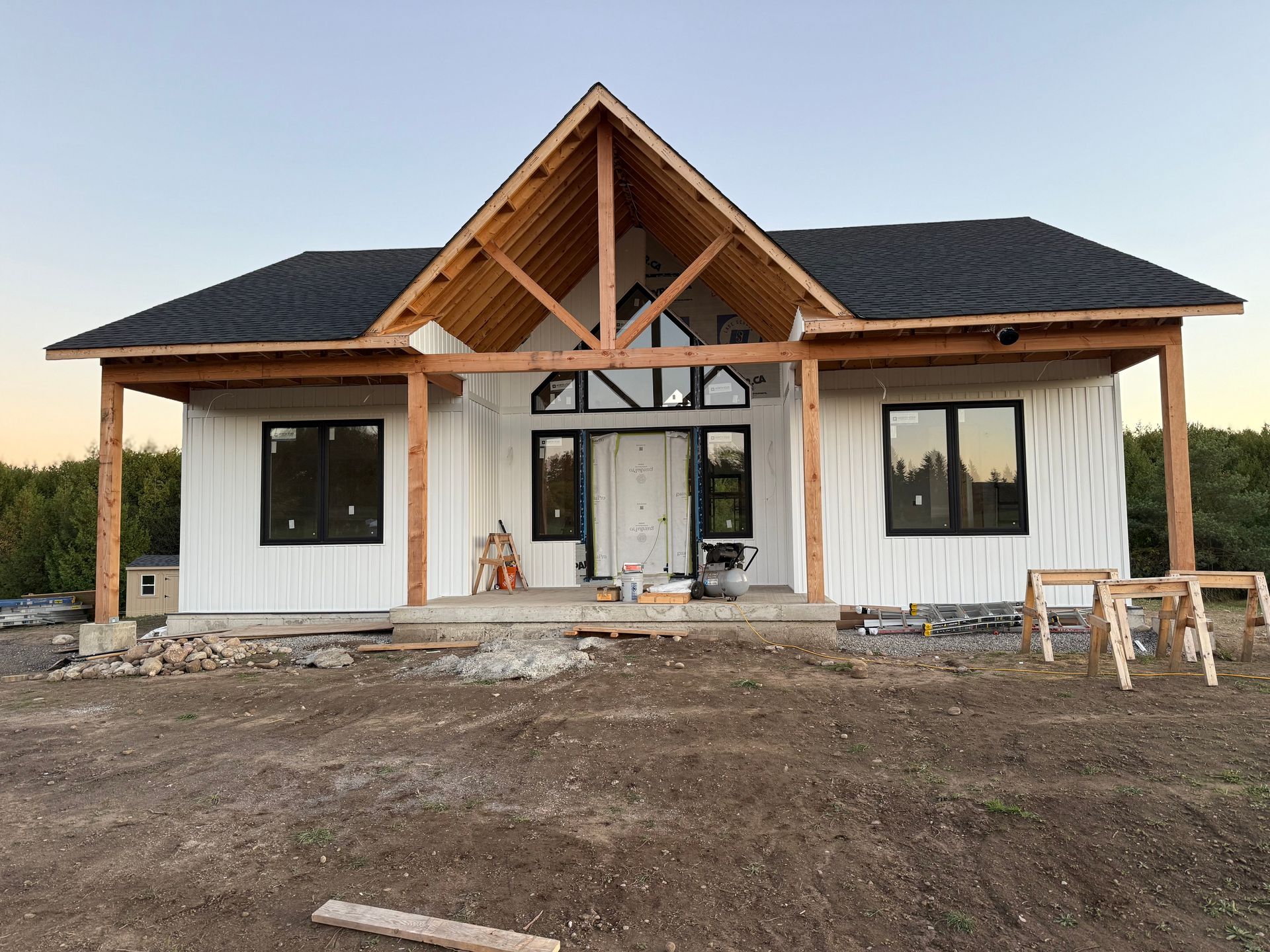 Front view of a newly built house with white siding, dark roof, and exposed wooden porch beams.
