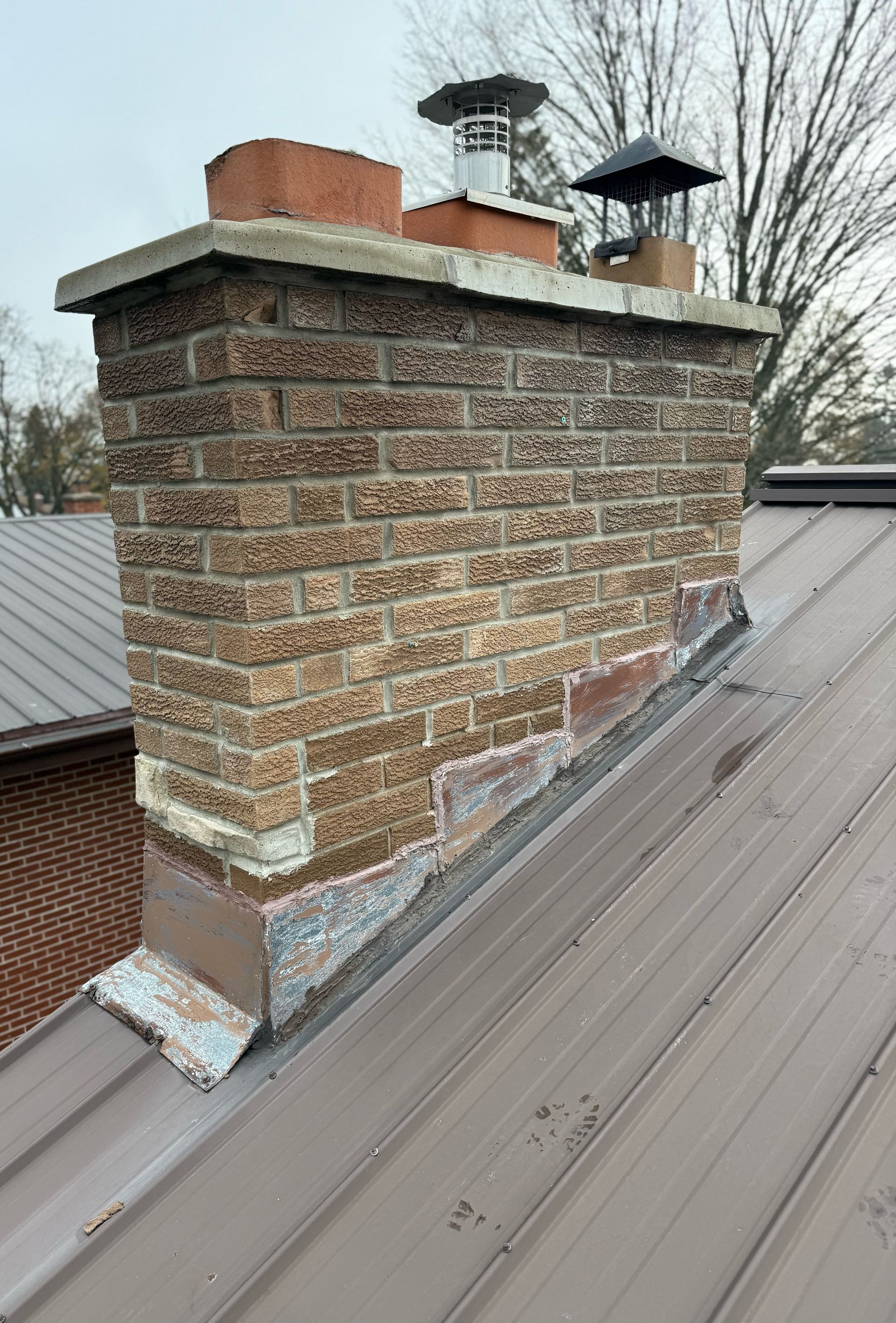 Brick chimney with two metal caps on a sloped metal roof under cloudy sky