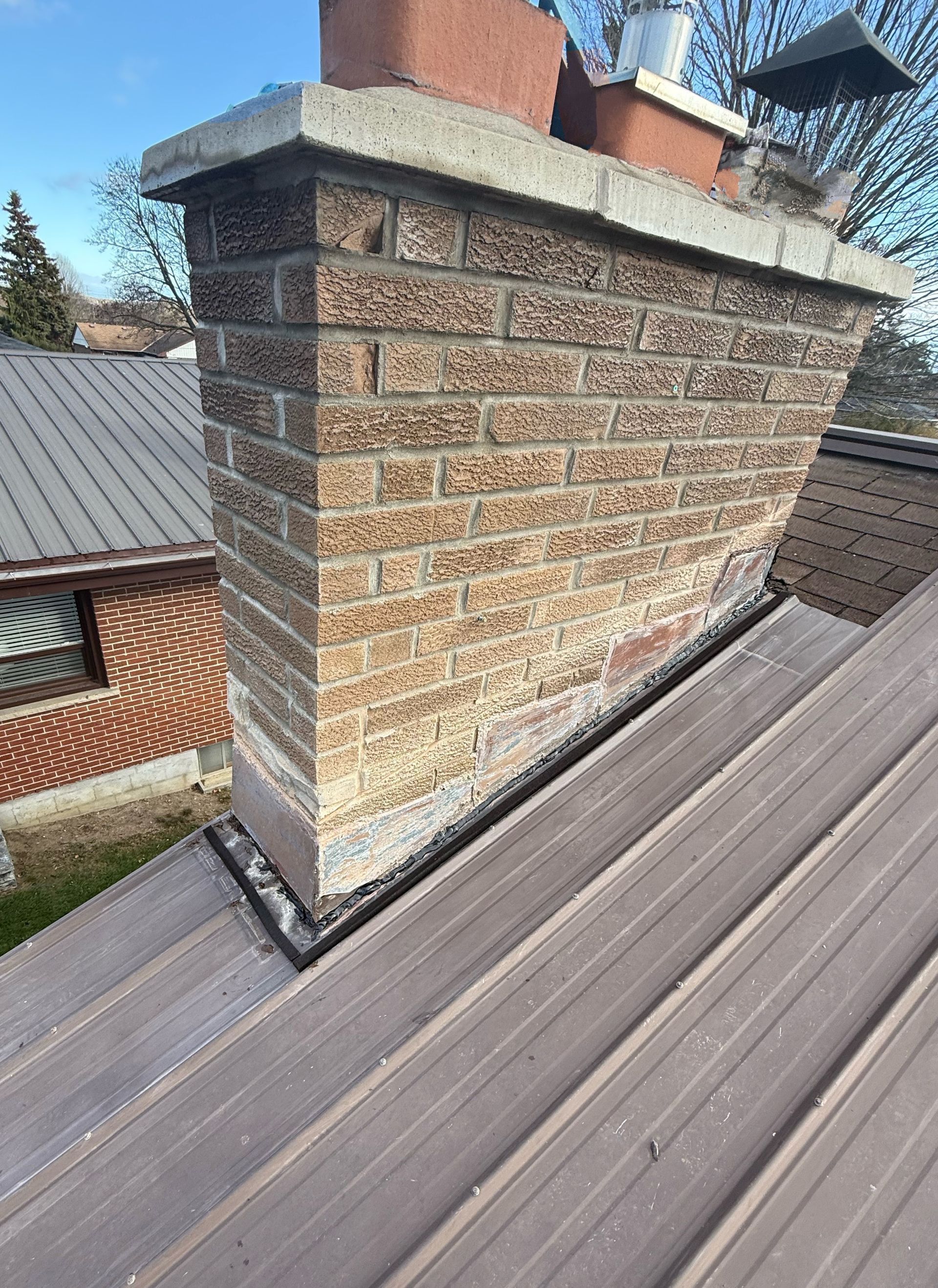 Brick chimney on a sloped roof with a metal cap and weathered shingles