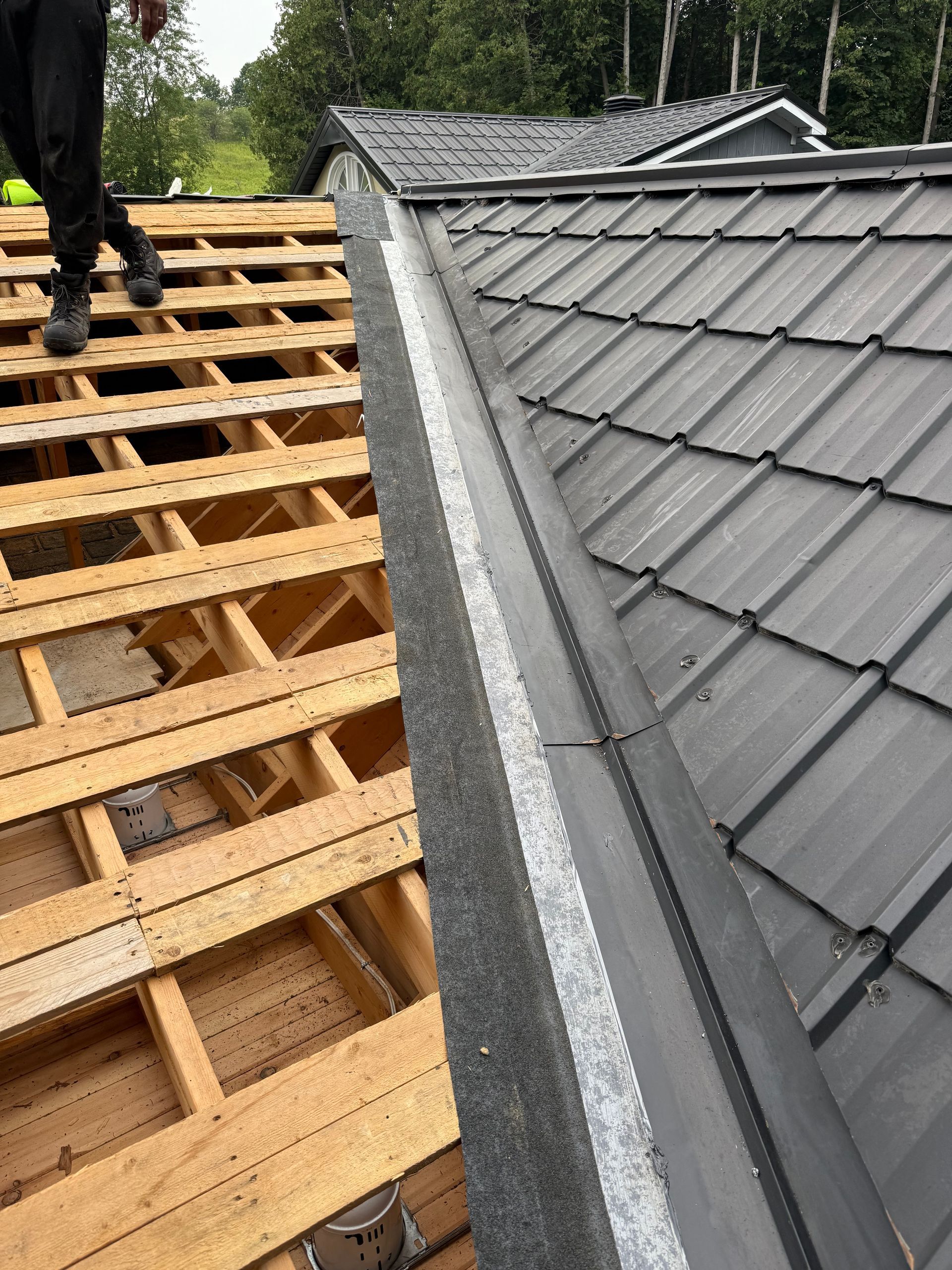 Roofing work with exposed wooden battens beside a gray tiled roof and a worker on the left