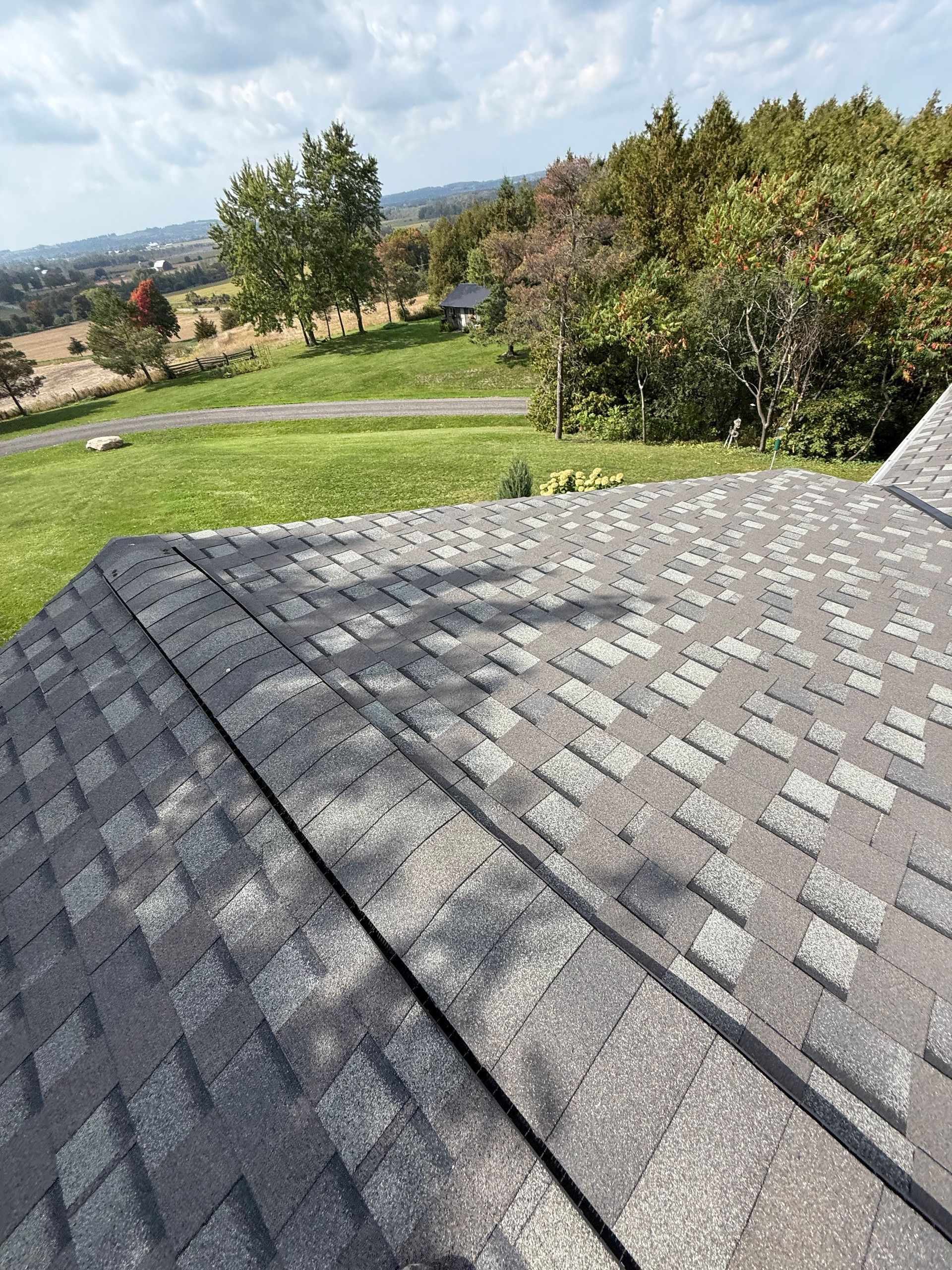 Gray shingled roof overlooking a green yard and trees on a sunny day