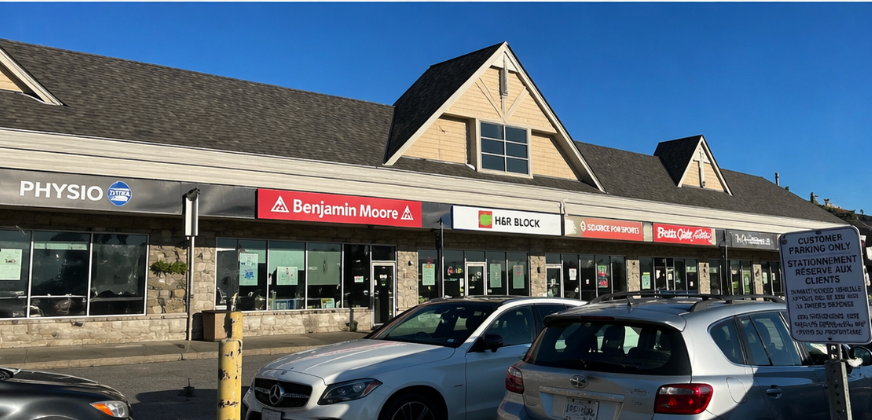 Strip mall storefronts under a blue sky, with parked cars in front and signs for Physio and Benjamin Moore.
