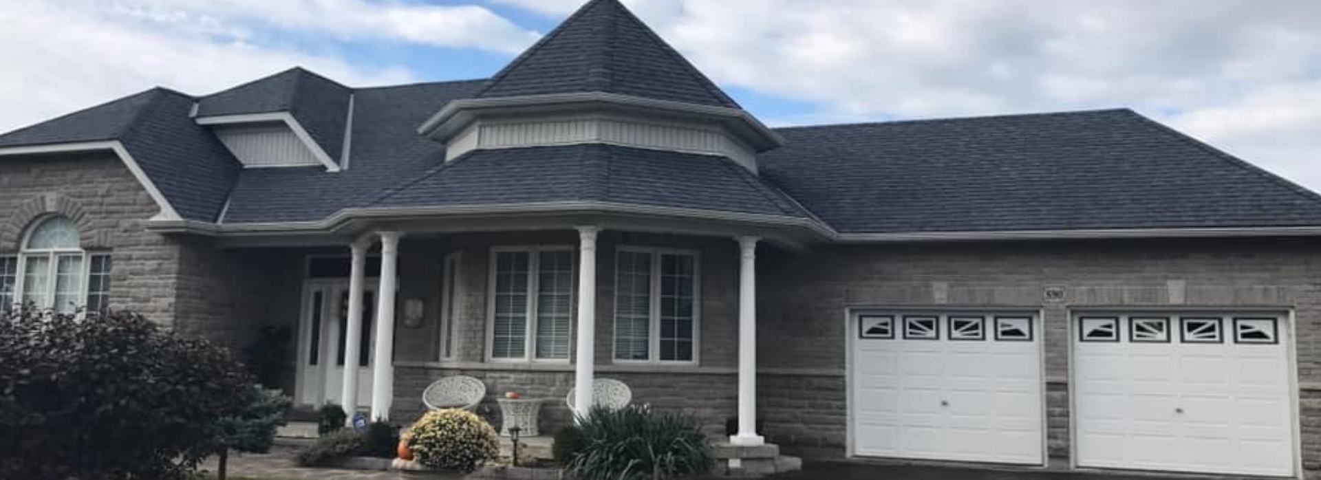 Single-story brick house with gray roof, white columns, and a two-car garage.