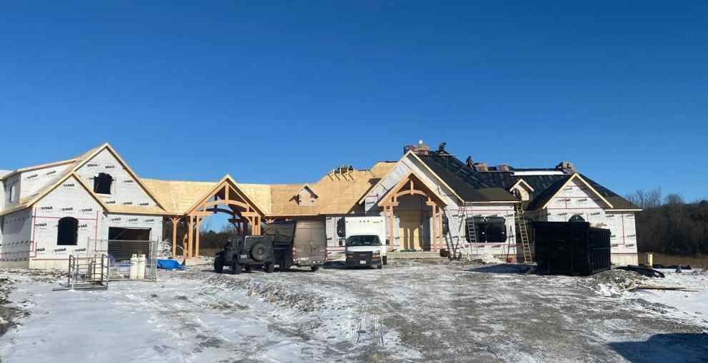 Partially built house with exposed framing in a snowy lot under a clear blue sky