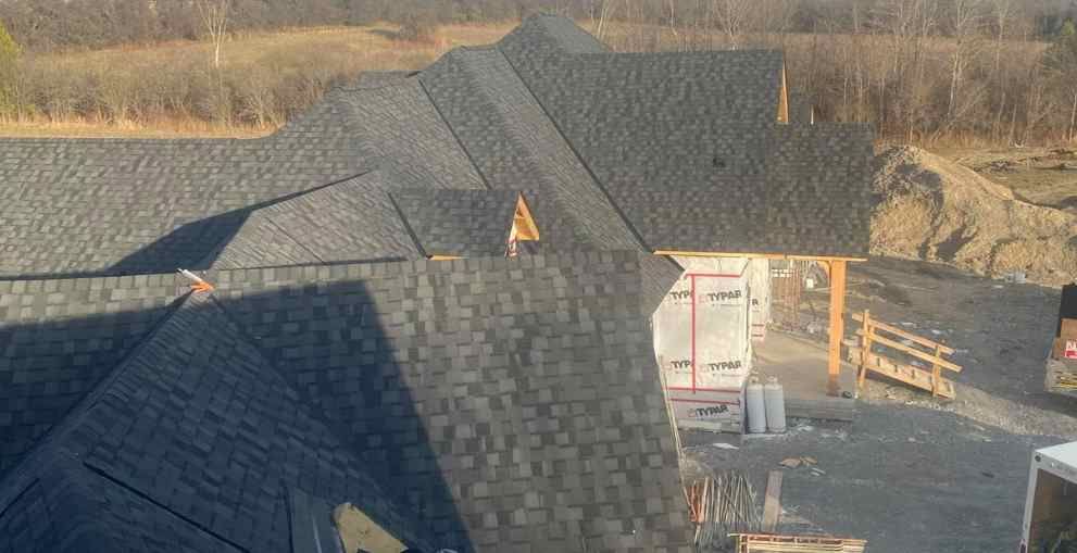 Aerial view of dark gray shingled rooftops under construction beside a wooded area.