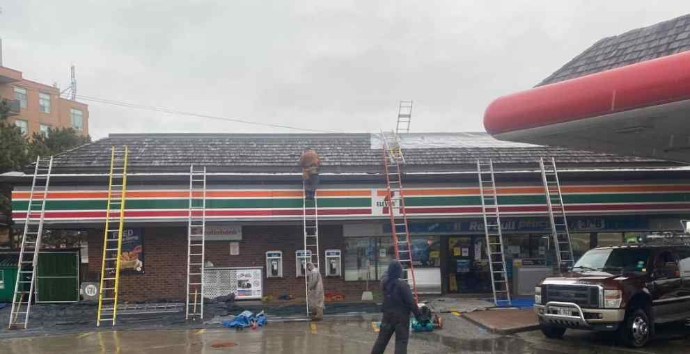 Storefront under renovation with colorful striped facade, ladders, workers, and a parked truck in front.