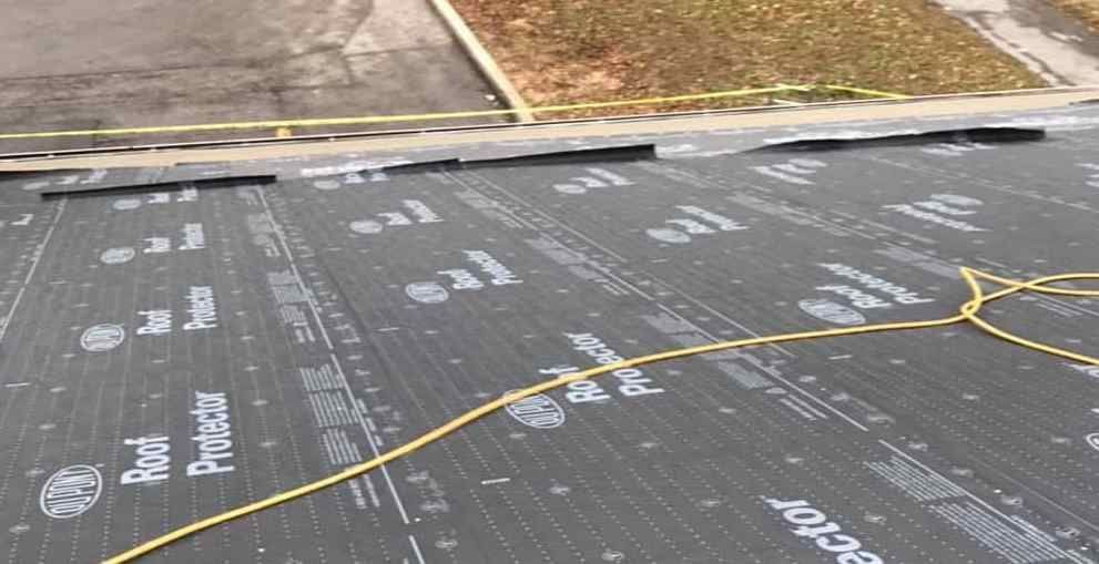 Roof with black waterproof membrane and a yellow hose or cable running across it, near a paved curb.