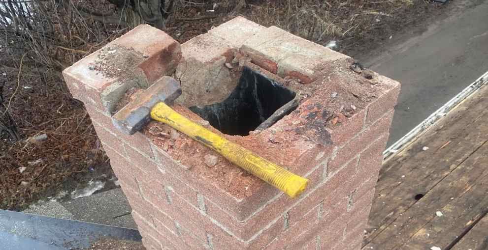 Hammer resting on a damaged brick chimney with a hole in the top