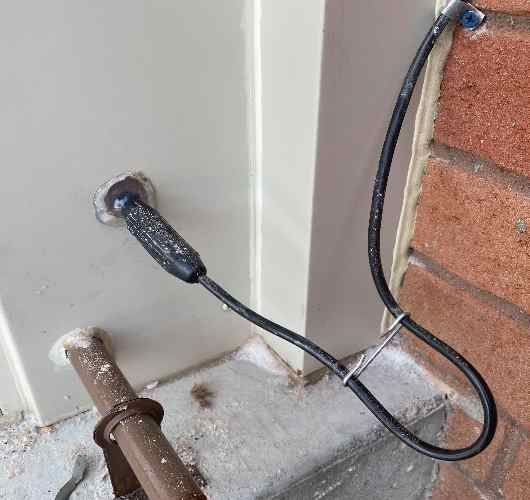 Electrical cables running from a wall opening beside a brick wall and pipe in a construction area