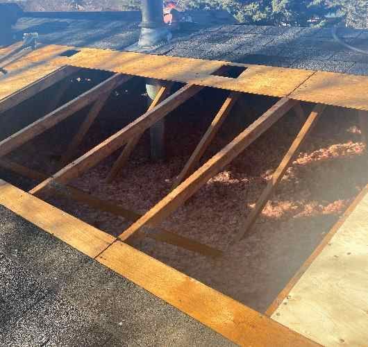Wooden deck hatch open over a dark pit, with angled supports and smoke or dust in the background