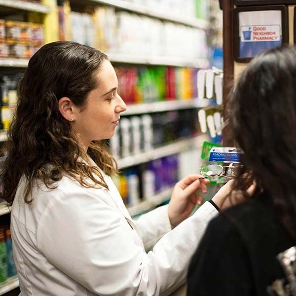 Woman in a store aisle comparing products on a shelf, holding a green and white package.