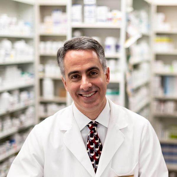 Smiling pharmacist in a white lab coat standing in a pharmacy aisle