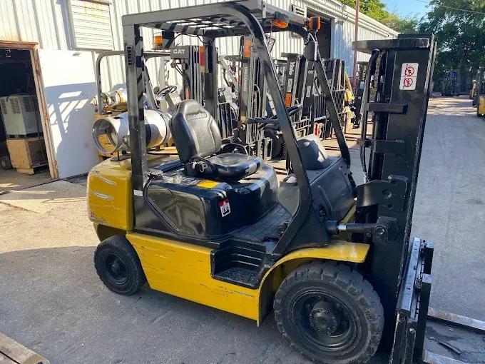 Yellow forklift parked outdoors in an industrial yard, side view with raised mast.