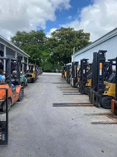 Forklifts parked along both sides of a warehouse driveway under a cloudy sky.