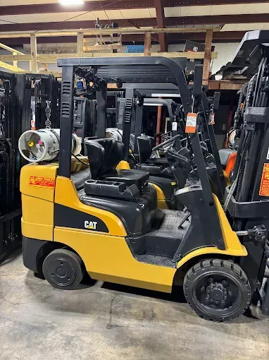 Yellow CAT forklift parked indoors in a warehouse, with another forklift in the background.