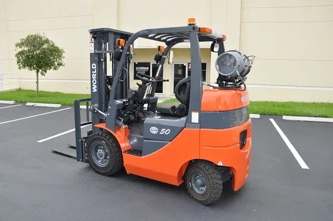 Orange forklift parked in an empty lot beside a beige building