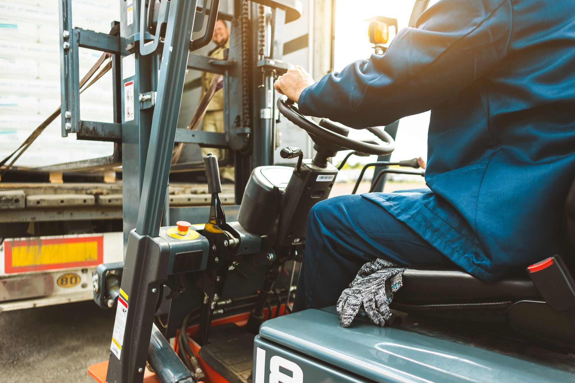 Forklift operator in blue jacket steering a forklift beside a truck loading area.