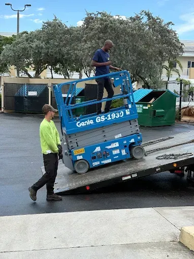 Workers loading a blue Genie boom lift onto a flatbed trailer outdoors.