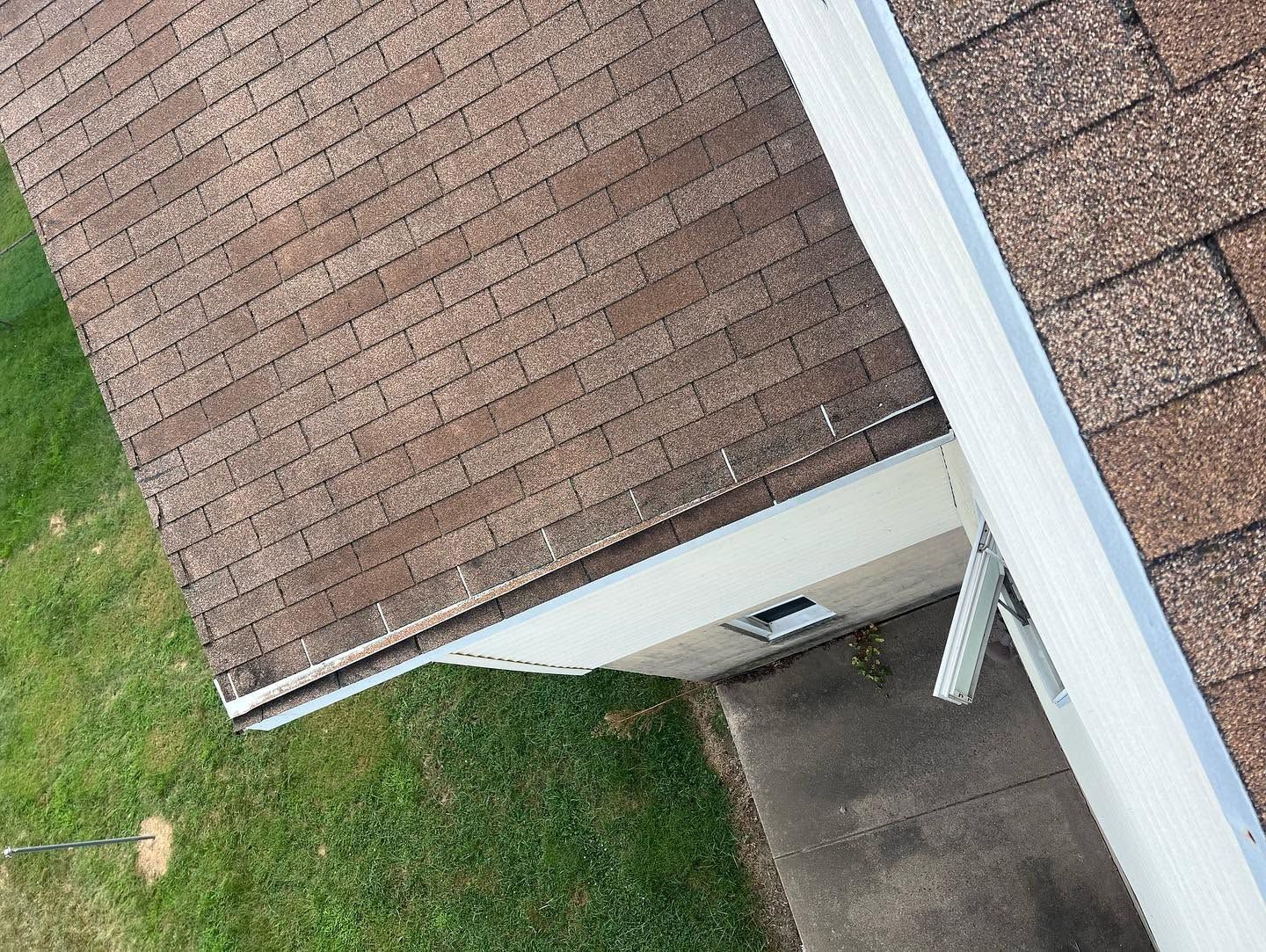 Aerial view of a house roof, white siding, and a driveway beside a grassy lawn.