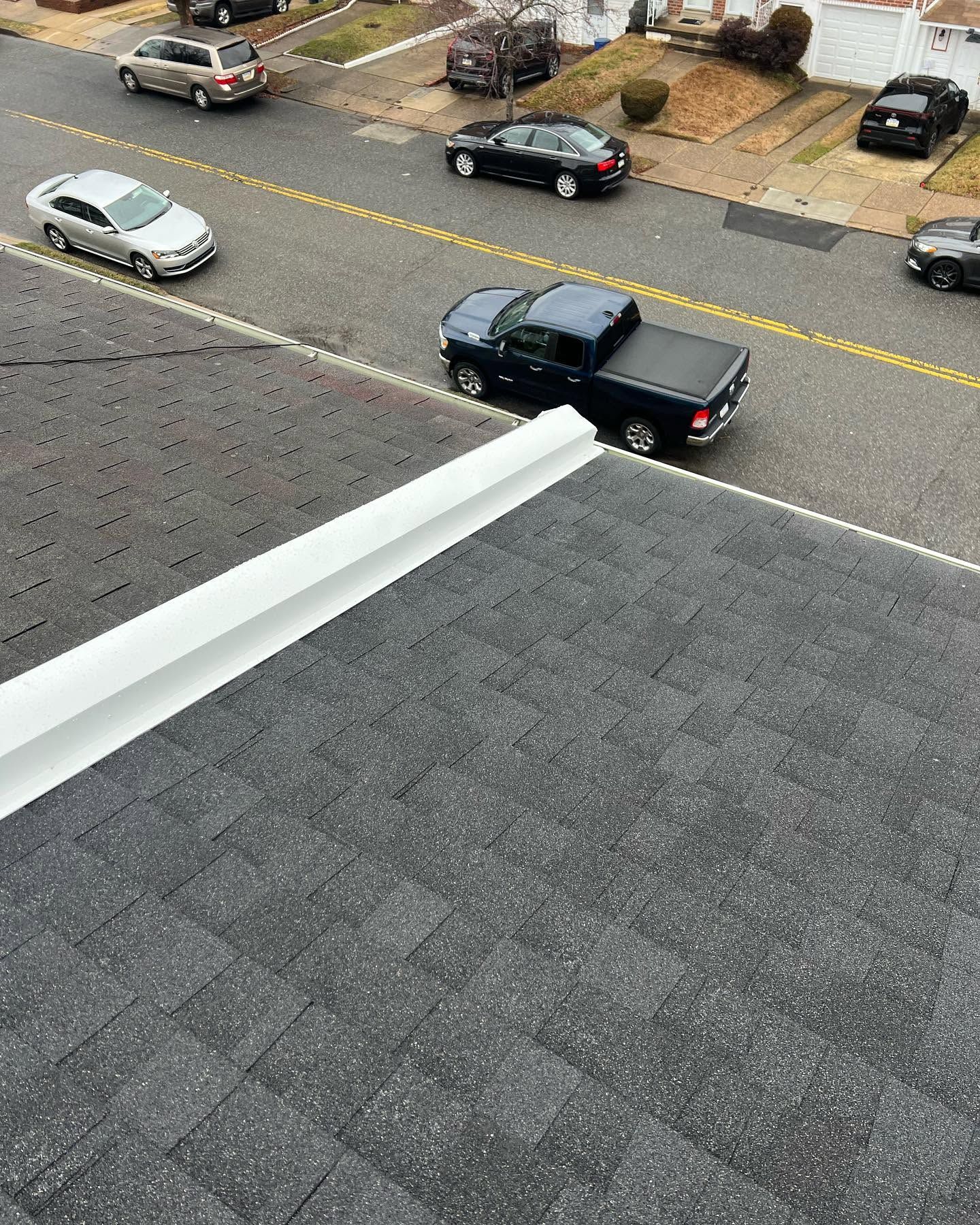 Black pickup truck driving on a residential street below a shingled roof edge.