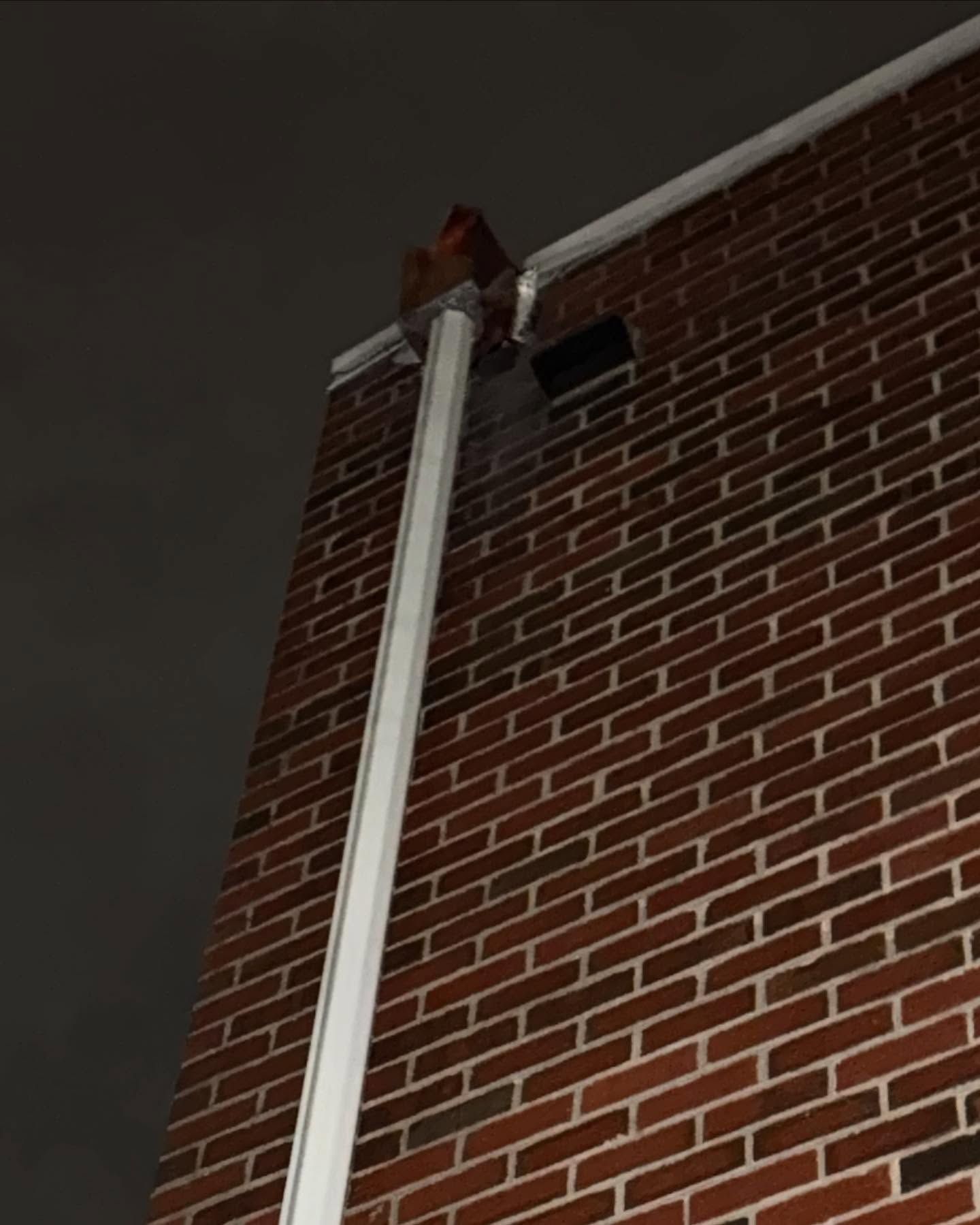 Tall white pipe mounted on a red brick building at night