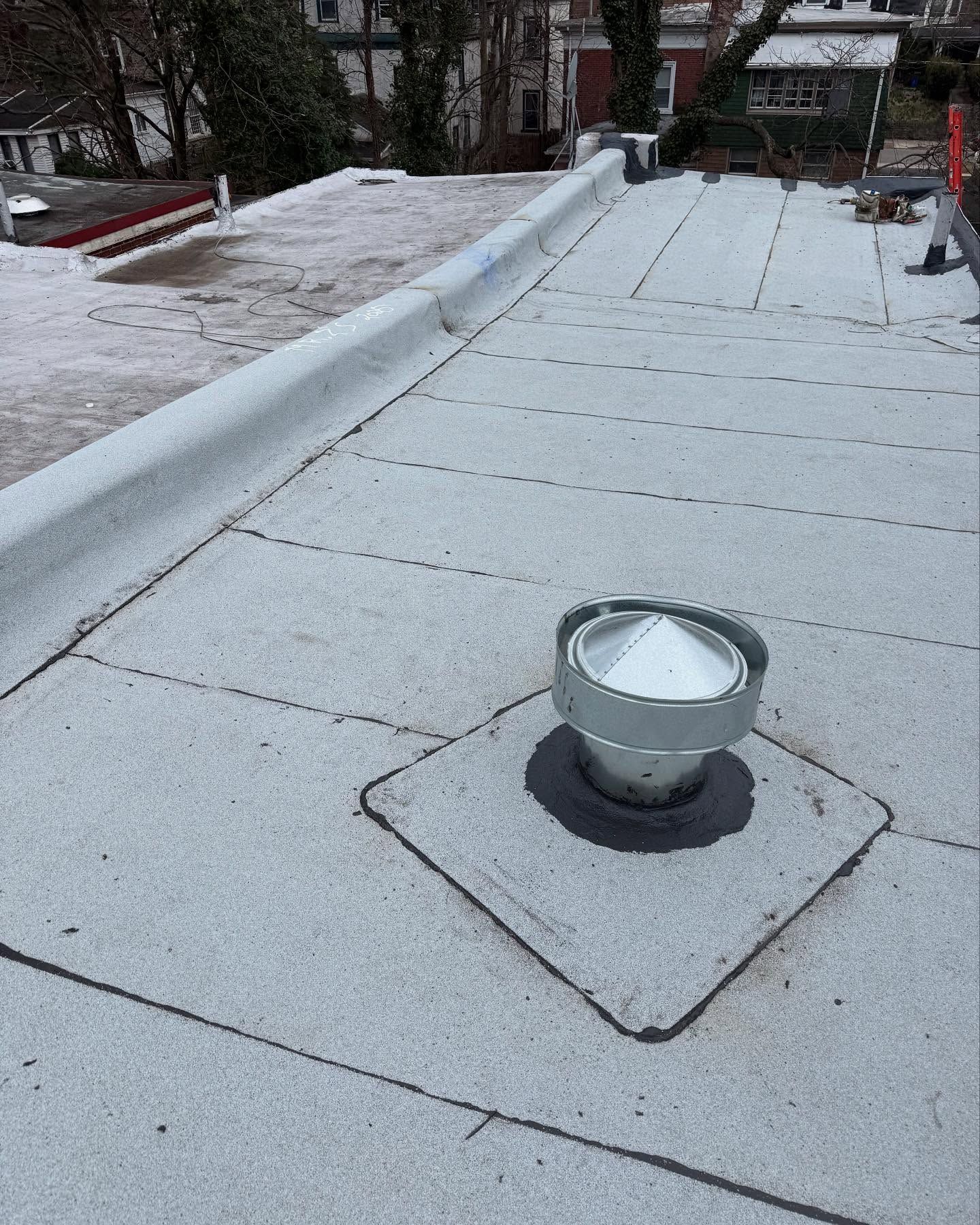 Flat gray rooftop with a vent in the foreground and snow along the edges.
