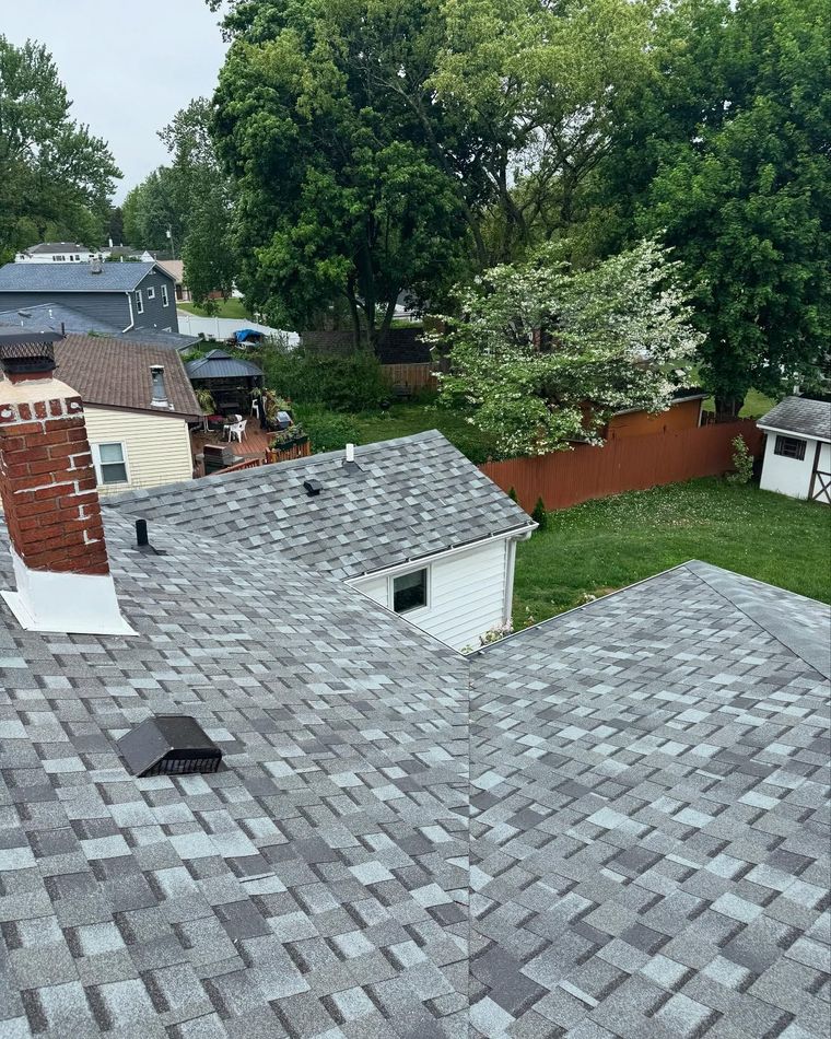 Gray shingled rooftops overlooking a backyard with trees and a red fence