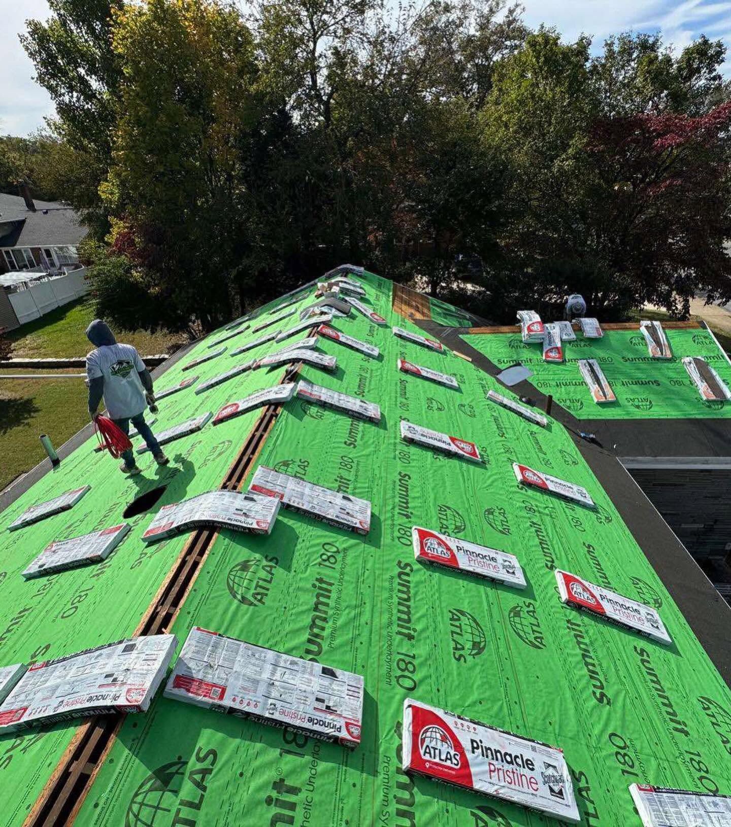 Workers installing bright green roofing underlayment on a sloped roof outdoors