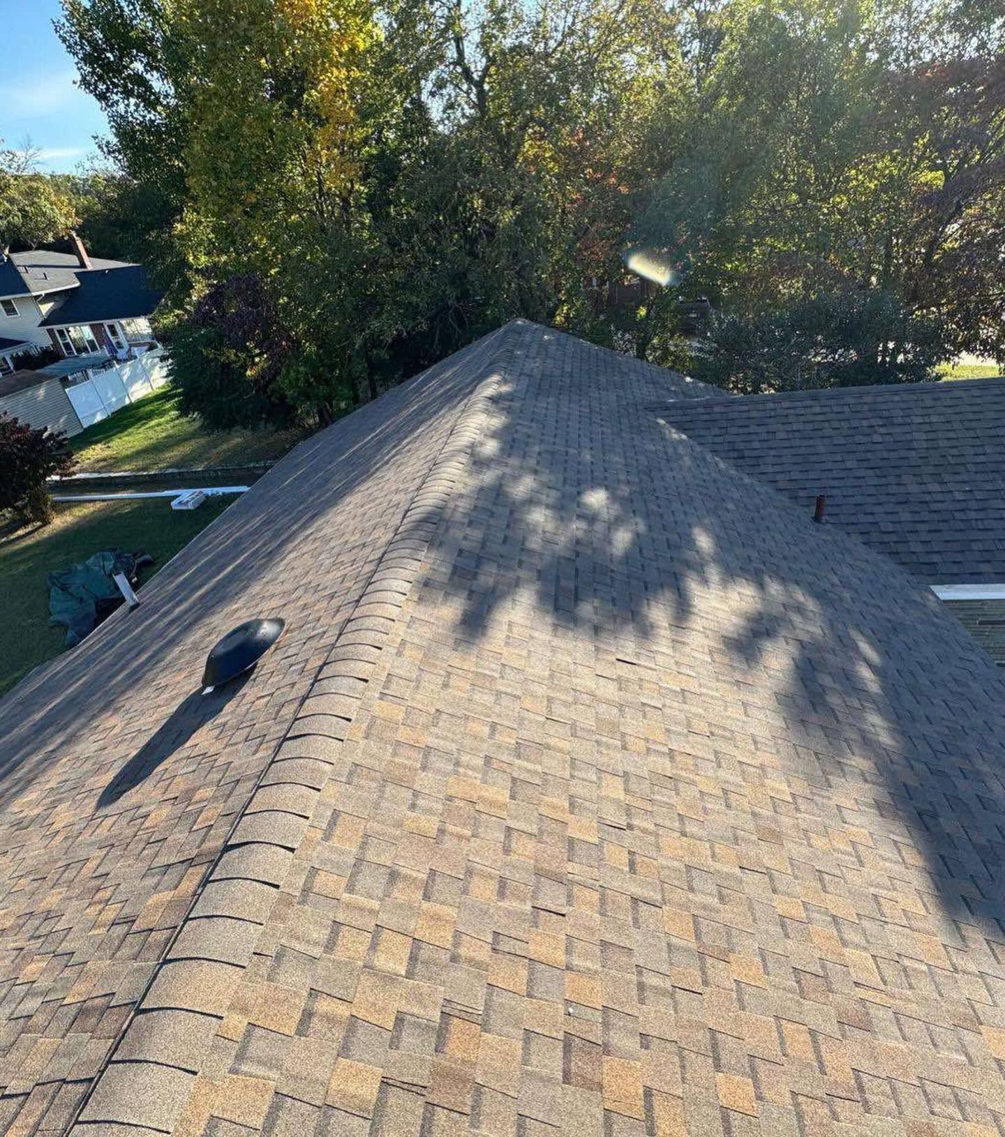 Aerial view of a shingled house roof with tree shadows and neighboring homes in the background