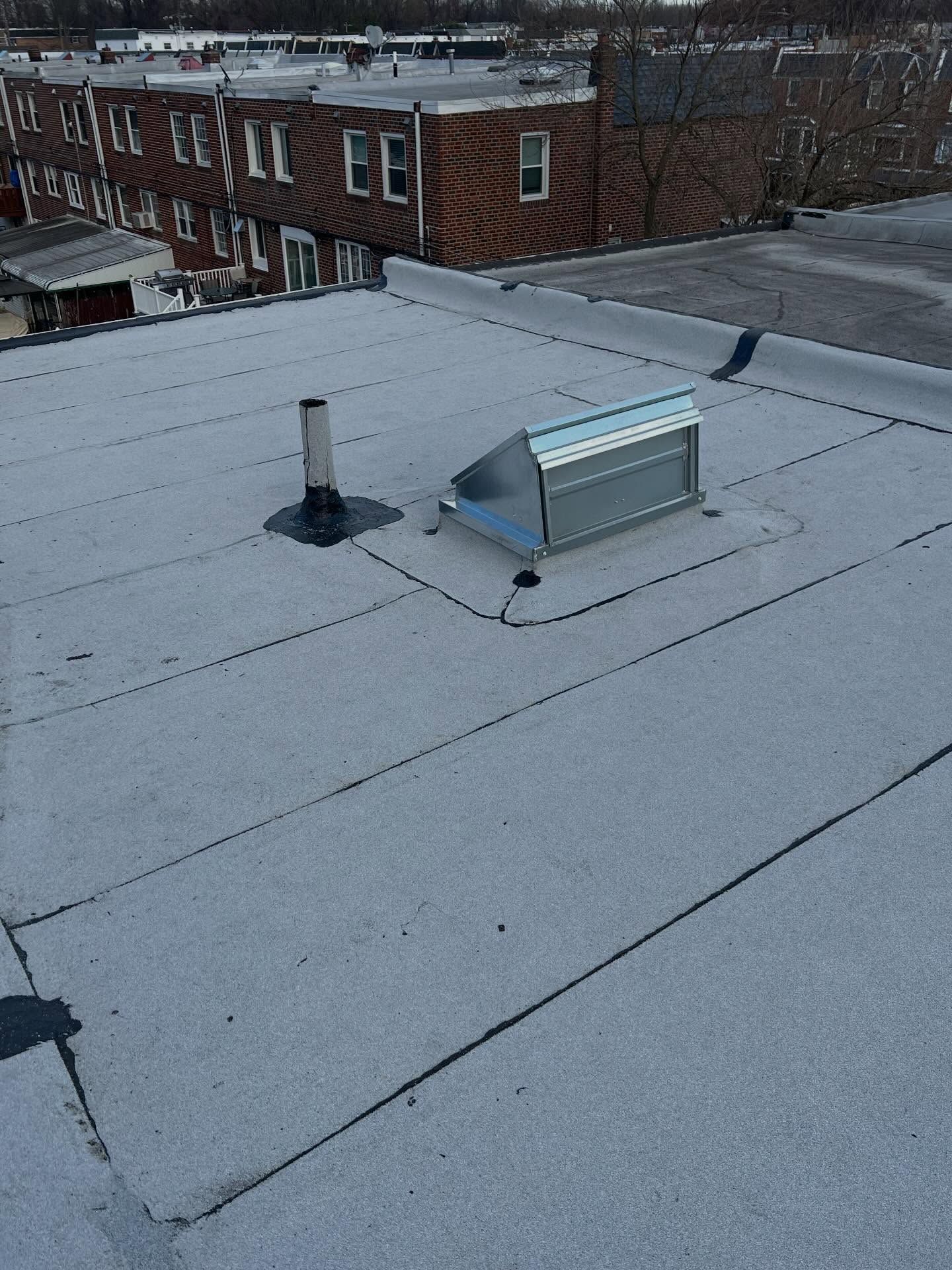 Flat rooftop with two metal vents and neighboring brick buildings in the background.