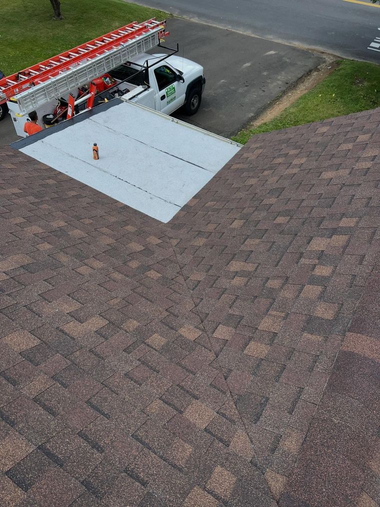 Utility truck with ladder parked on a driveway beside a curb ramp and traffic cone.