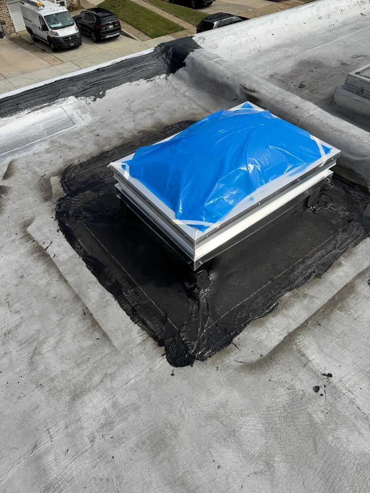Rooftop ventilation unit covered with a blue tarp on a black waterproofed base.