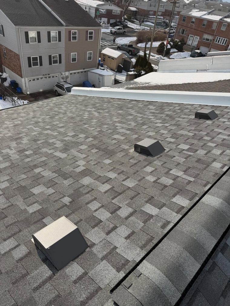 Snowy rooftop with gray shingles, skylights, and nearby suburban houses in the background