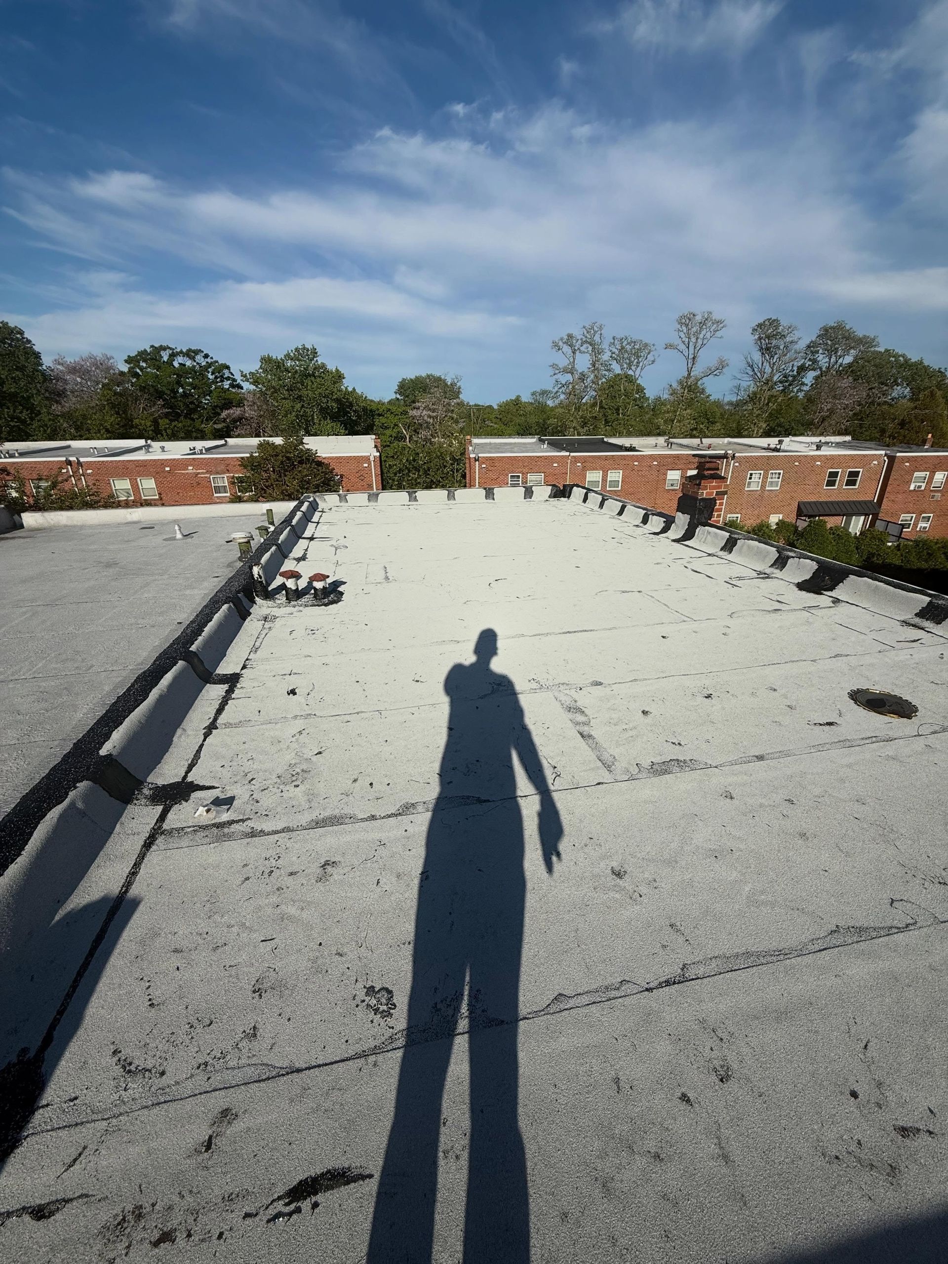 Rooftop covered in gravel under a blue sky, with a person’s shadow in the foreground.