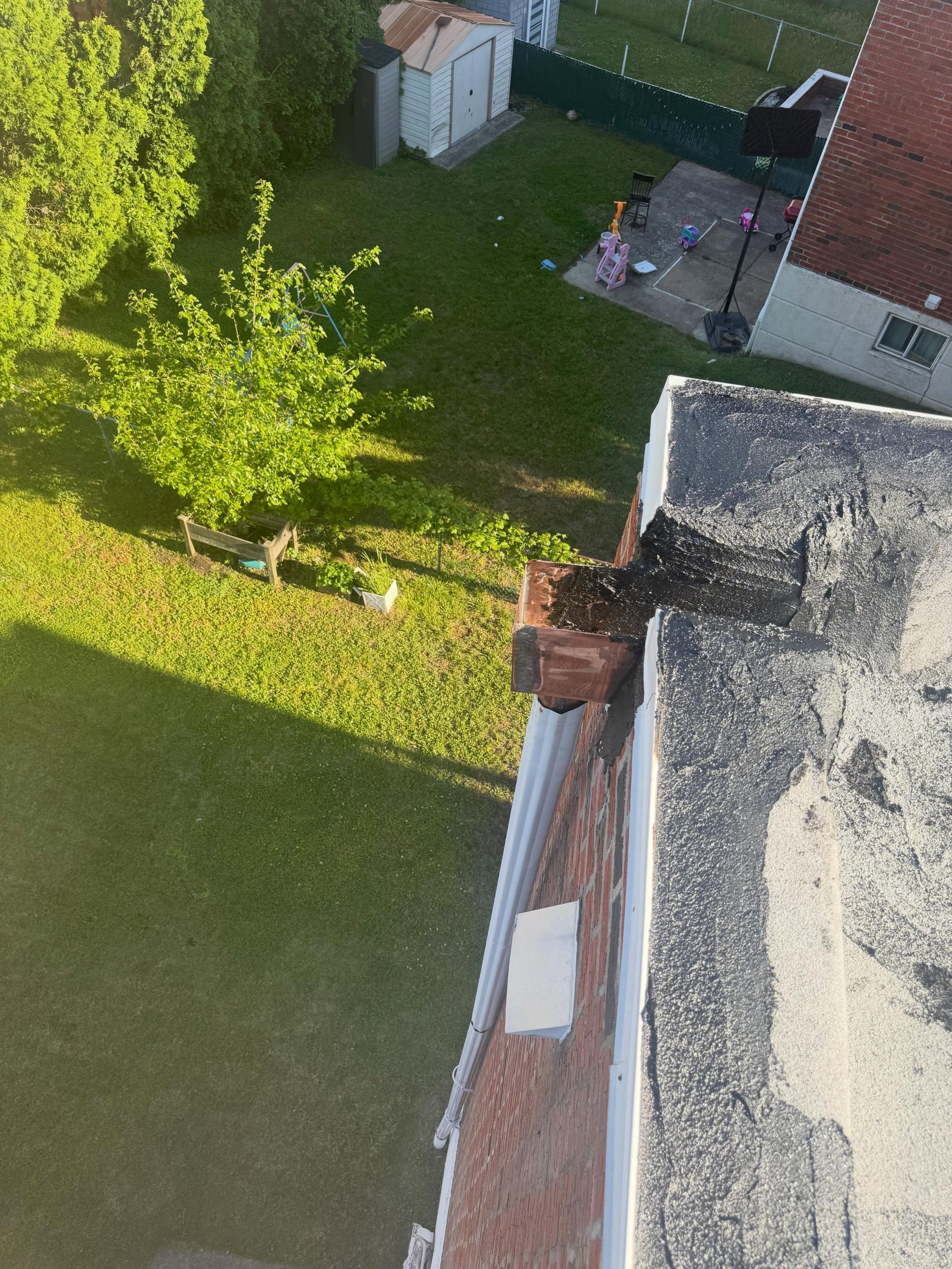Aerial view of a grassy yard with a tree, patio furniture, and part of a brick-roofed building.