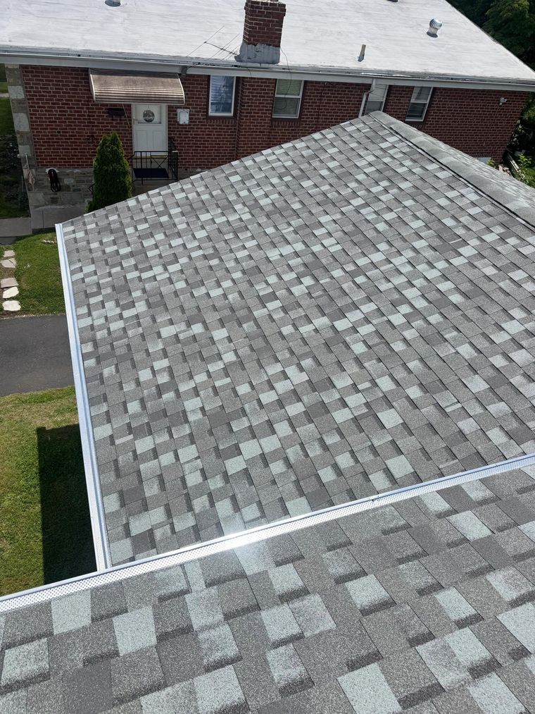 Aerial view of a gray shingled roof beside a red brick house and lawn