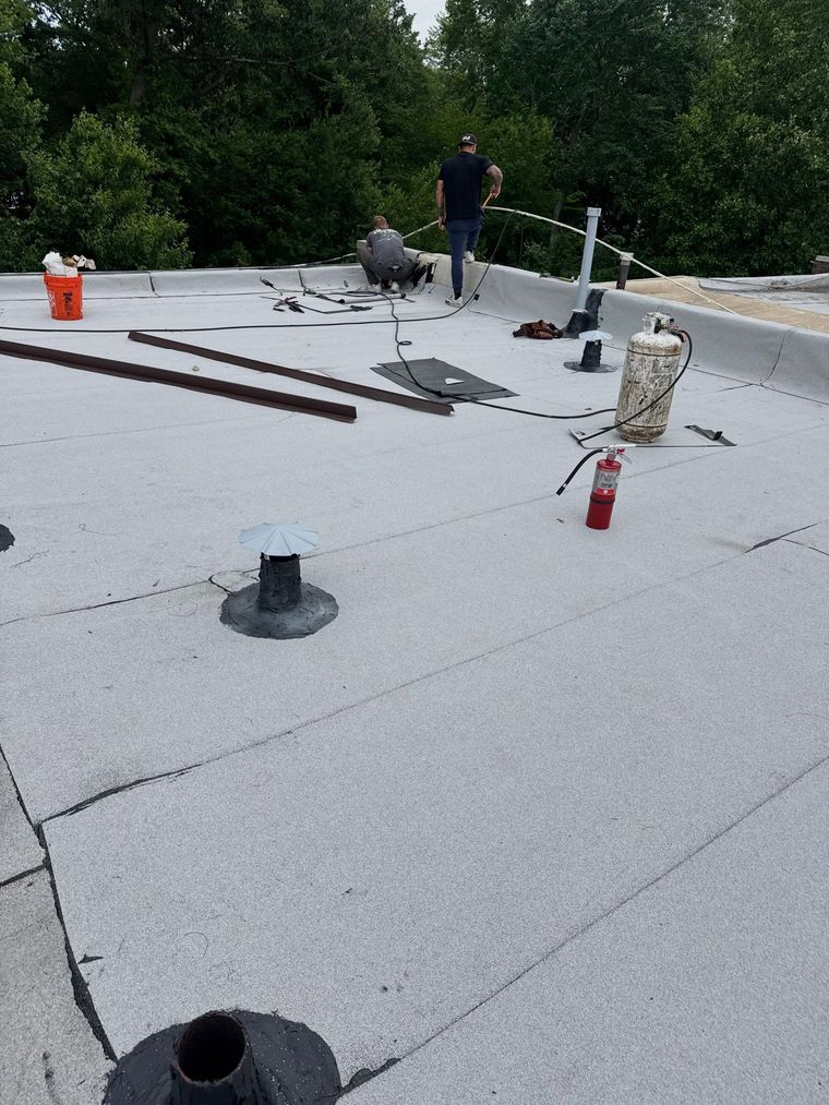 Flat rooftop with roofing materials, vents, and a worker near the far edge.